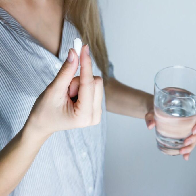 woman holding half full glass and white medicine pill
